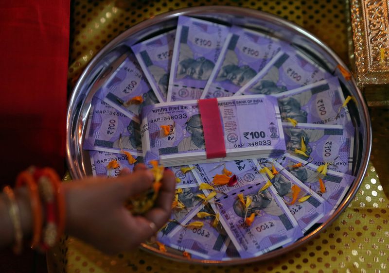 © Reuters. FILE PHOTO: A woman puts flower petals on the new 100 Indian rupee notes as she prays as part of a ritual during Dhanteras, a Hindu festival associated with Lakshmi, the goddess of wealth, in Ahmedabad, India, November 5, 2018. REUTERS/Amit Dave/File Photo