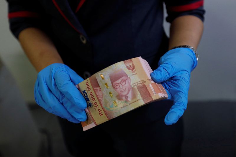 © Reuters. Seorang karyawan mengenakan sarung tangan sintetis saat menghitung uang kertas rupiah di kantor penukaran mata uang di Jakarta, Indonesia, 19 Maret 2020. REUTERS/Willy Kurniawan/Files