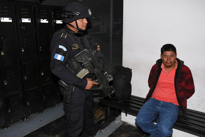 © Reuters. FILE PHOTO: A police officer stands next to Rigoberto Ramon Miranda Orozco, suspected on smuggling charges over the deaths of 53 migrants on a sweltering truck in Texas in 2022, at a court in Guatemala City, Guatemala, August 21, 2024. REUTERS/Stringer/File photo