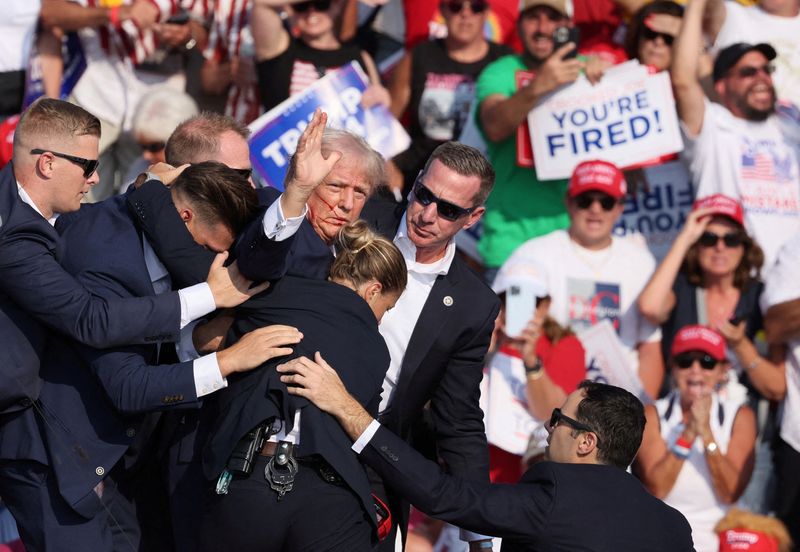 &copy; Reuters. O candidato presidencial republicano e ex-presidente dos EUA, Donald Trump, gesticula com o rosto ensanguentado enquanto é auxiliado por funcionários do Serviço Secreto dos EUA após ser sido baleado na orelha direita durante comício no Butler Farm Sh