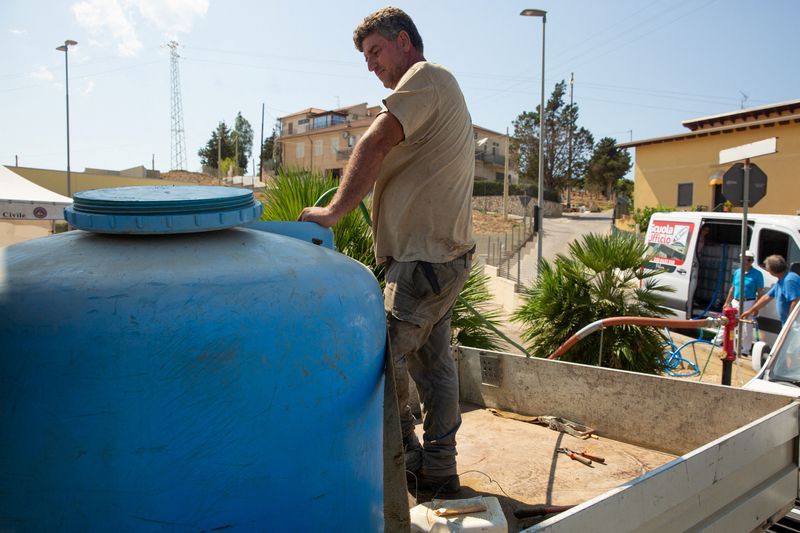 © Reuters. A man attaches water pipe to a tanker amidst water shortages in Sicilan town of Alcamo, Italy, August 8, 2024. REUTERS/Antonio Cascio