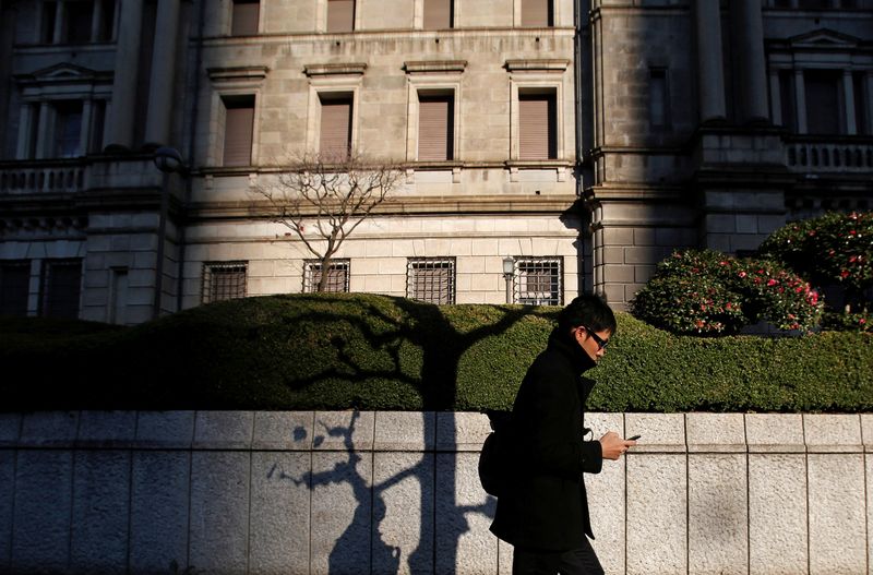 © Reuters. FILE PHOTO: A man using his mobile phone walks past the Bank of Japan headquarters building in Tokyo December 19, 2014. REUTERS/Yuya Shino /File Photo