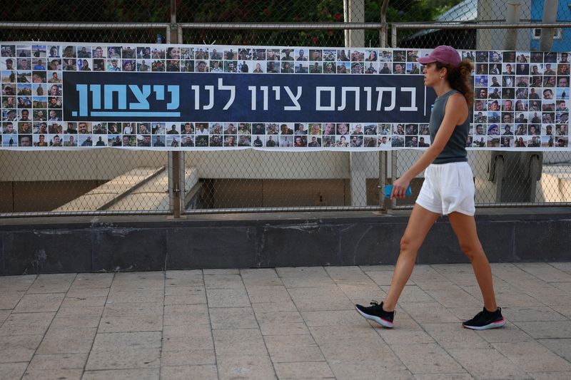 © Reuters. A woman walks past a banner depicting the faces of Israel’s fallen soldiers, amid the ongoing conflict in Gaza between Israel and Hamas, in Tel Aviv, Israel, August 19, 2024. REUTERS/Florion Goga/ File Photo