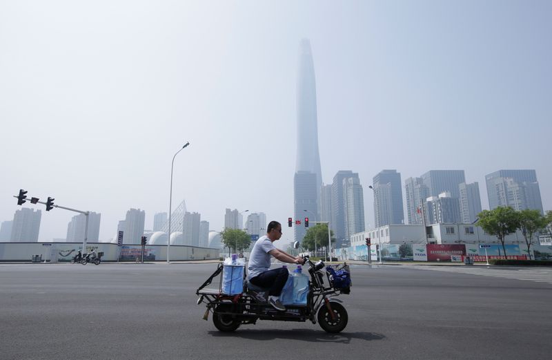 © Reuters. FILE PHOTO: A man rides an electric motorcycle carrying water past the Chow Tai Fook Financial Center in Binhai New District in Tianjin, China, May 16, 2019. Picture taken May 16, 2019. REUTERS/Jason Lee/File Photo