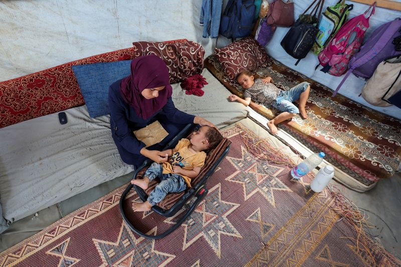 © Reuters. FILE PHOTO: The mother of Palestinian boy Abdul Rahman Abu Al-Jidyan, who is the first person to contract polio in Gaza in 25 years, looks after him in their tent, in Deir Al-Balah, in the central Gaza Strip August 28, 2024. REUTERS/Ramadan Abed/File Photo