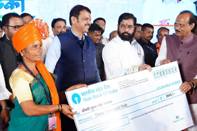 © Reuters. FILE PHOTO: Maharashtra Chief Minister Eknath Shinde accompanied by his deputies Devendra Fadnavis and Ajit Pawar hands a symbolic cheque to a beneficiary of a government welfare scheme, in Kinhi, Maharshtra, India August 24, 2024.   Devendra Fadnavis via X/Handout via REUTERS/File Photo