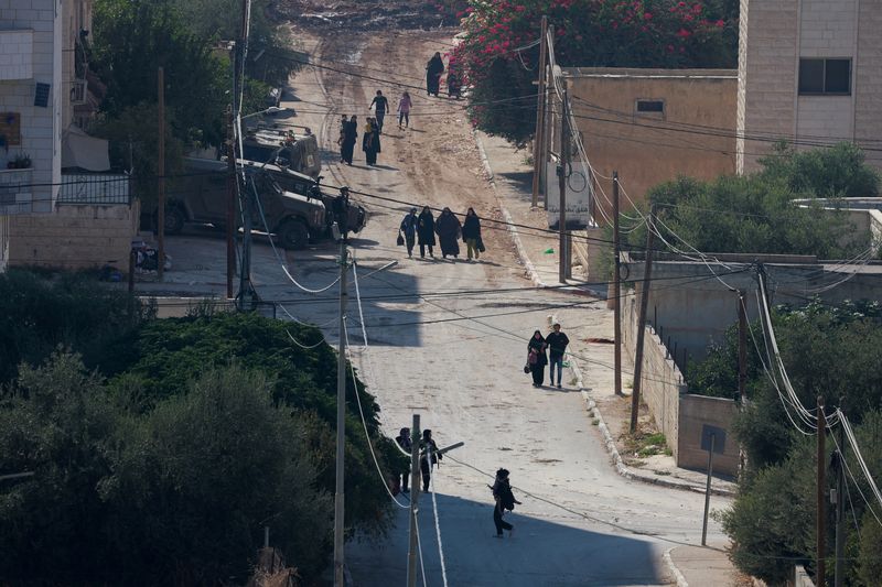 © Reuters. Palestinians walk near Israeli military vehicles, during an Israeli raid in Jenin, in the Israeli-occupied West Bank, August 31, 2024. REUTERS/Ammar Awad