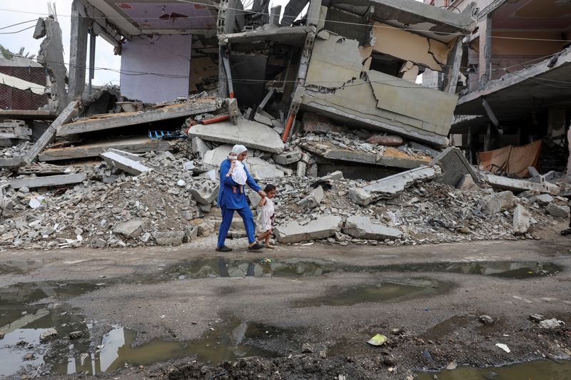 © Reuters. A displaced Palestinian mother, Wafaa Abdelhadi, walks past the rubble of a house destroyed in an Israeli strike as she returns to her shelter with her daughters Lynn and Roueida, after they got vaccinated against polio, in Deir Al-Balah, in the central Gaza Strip September 1, 2024. REUTERS/Ramadan Abed