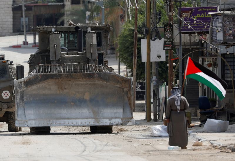 © Reuters. A man holding a Palestinian flag stands in front of Israeli military vehicles during an Israeli raid in Tulkarm, in the Israeli-occupied West Bank, September 3, 2024. REUTERS/Mohammed Torokman 