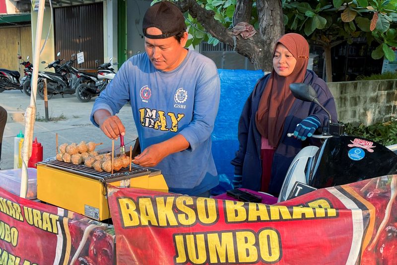 © Reuters. Rahmat Hidayat, 44 tahun, melayani pelanggan sambil memanggang bakso setelah kehilangan pekerjaannya saat pabrik sepatu tempatnya bekerja tutup tahun lalu di Karawang, Provinsi Jawa Barat, Indonesia, 31 Juli 2024. REUTERS/Stefanno Sulaiman