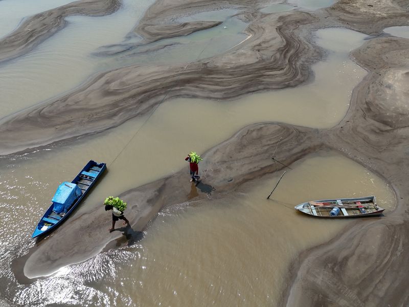 &copy; Reuters. Pessoas carregam bananas caminhando sobre bancos de arei em meio à seca que afeta o Rio Solimões, em Manacapuru, no Amazonasn14/09/2024 REUTERS/Bruno Kelly