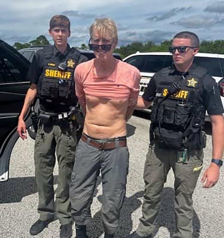 © Reuters. Ryan W. Routh, suspected of attempting to assassinate Republican presidential nominee and former U.S. President Donald Trump at his West Palm Beach golf course, stands handcuffed between two Martin County Sheriff's office deputies after his arrest during a traffic stop near Palm City, Florida, U.S., September 15, 2024.  Martin County Sheriff's Office/Handout via REUTERS   