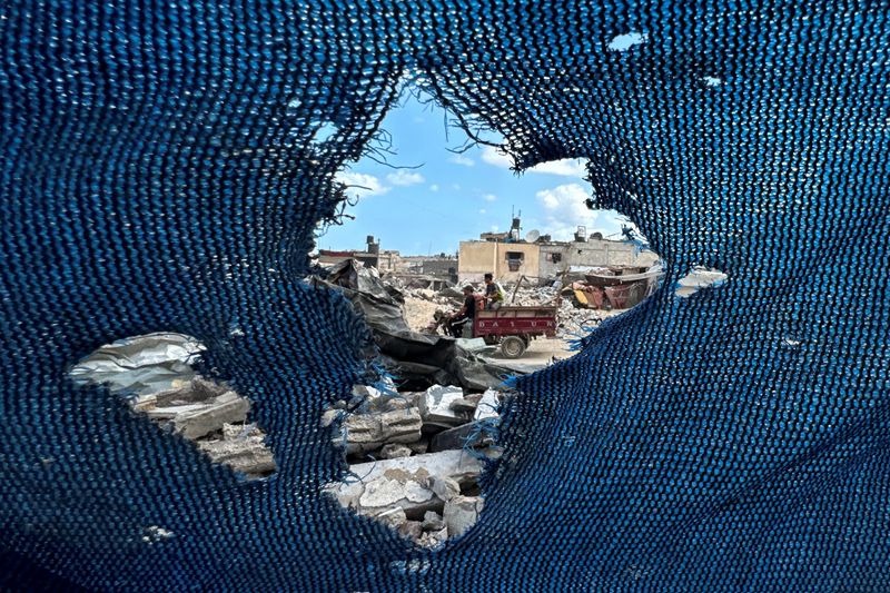 © Reuters. Palestinians, seen through a torn tent, ride a motorized vehicle past the rubble, amid the Israel-Hamas conflict, in Khan Younis, in the southern Gaza Strip, September 16, 2024. REUTERS/Mohammed Salem   