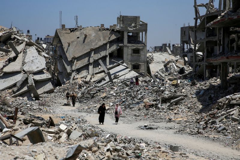 © Reuters. FILE PHOTO: Palestinians walk past the rubble of houses destroyed during the Israeli military offensive, amid Israel-Hamas conflict, in Khan Younis in the southern Gaza Strip July 10, 2024. REUTERS/Hatem Khaled/File Photo