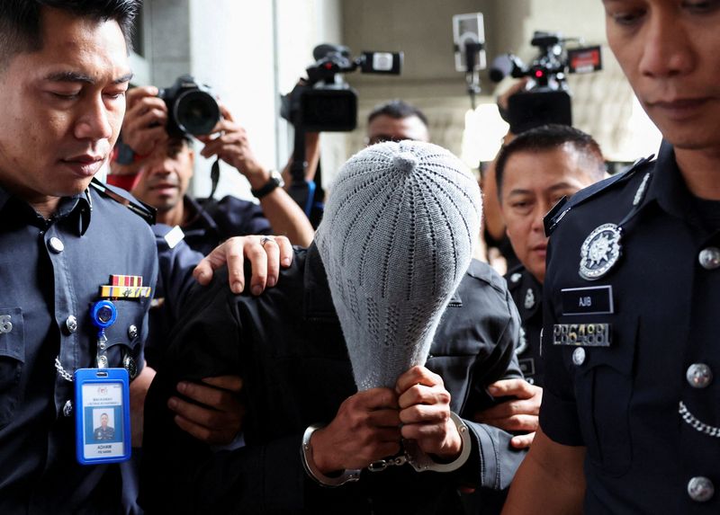 © Reuters. A man linked to Global Ikhwan Service and Business Holdings (GISB) covers his face as he is escorted by police officers after being charged in a court in Putrajaya, Malaysia September 18, 2024. REUTERS/Hasnoor Hussain