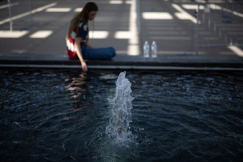 © Reuters. FILE PHOTO: A woman wearing a U.S. flag shirt sits by a a water fountain as temperatures are expected to soar above 110 degrees Fahrenheit (43.3 degrees Celsius) during the summer's first heat wave, in Phoenix, Arizona, U.S., June 6, 2024. REUTERS/Carlos Barria/File Photo