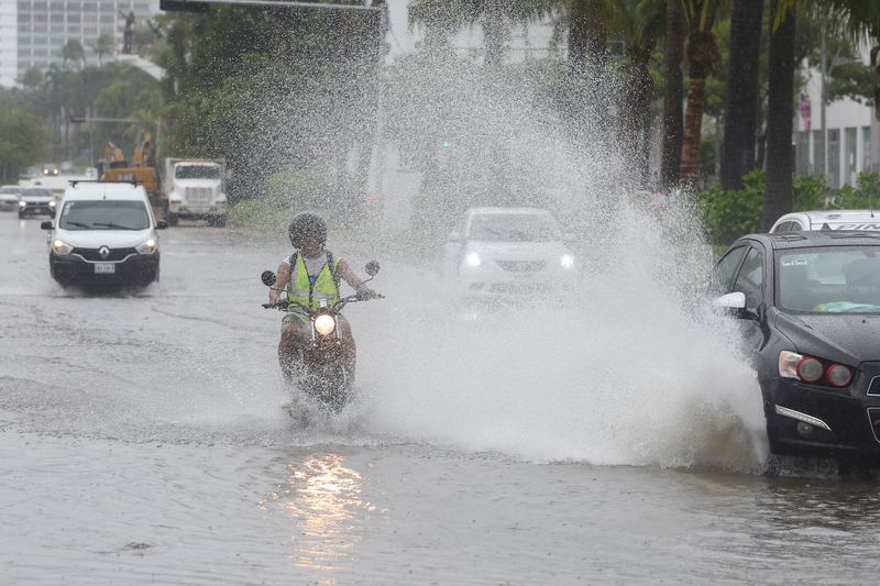 &copy; Reuters. A motorist is splashed by a car driving through a flooded street in the aftermath of Hurricane John in Acapulco, Mexico September 24, 2024. REUTERS/Javier Verdin