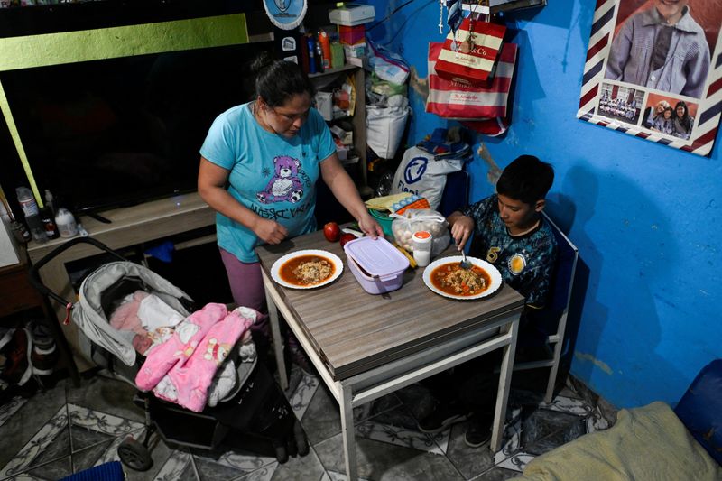 © Reuters. Lilian Gonzalez, 36, prepares a meal with the food she received from a soup kitchen, with her son, Joaquin Mendieta, 11, and her daughter, Dana Mendieta, in Villa Soldati, on the outskirts of Buenos Aires, Argentina September 16, 2024. REUTERS/Mariana Nedelcu