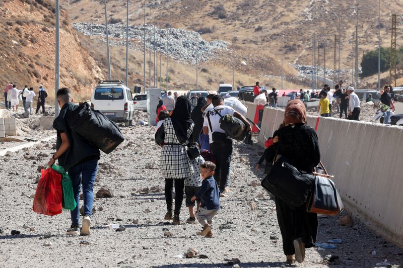 © Reuters. FILE PHOTO: People carry their belongings while walking on the rubble, after an Israeli strike, as they flee Lebanon due to ongoing hostilities between Hezbollah and Israeli forces, at Masnaa border crossing with Syria, in Lebanon, October 4, 2024. REUTERS/Mohamed Azakir/File Photo