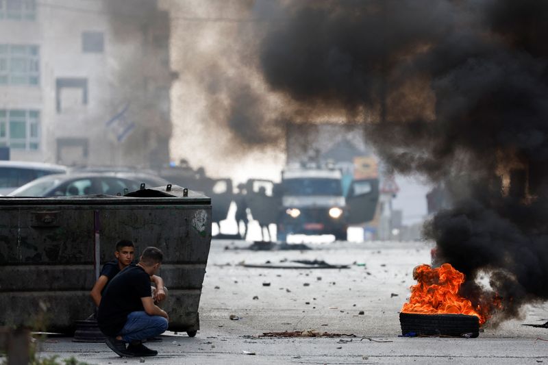 &copy; Reuters. Israeli soldiers stand next to military vehicles as Palestinians cover near a burning tire during an Israeli raid in Qalandya, in the Israeli-occupied West Bank, October 7, 2024. REUTERS/MohamadTorokman