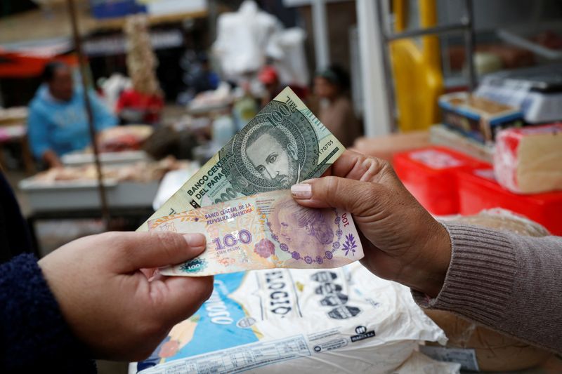 © Reuters. FILE PHOTO: A customer and a salesperson pose for a photograph while holding Argentine and Paraguayan bills at a market near the border with Argentina, in Nanawa, Paraguay May 16, 2024. REUTERS/Cesar Olmedo/File Photo