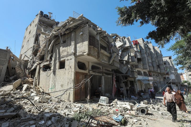 © Reuters. Palestinians walk past a house hit in an Israeli strike, amid the Israel-Hamas conflict, in Bureij refugee camp, in the central Gaza Strip, October 8, 2024. REUTERS/Ramadan Abed/File Photo