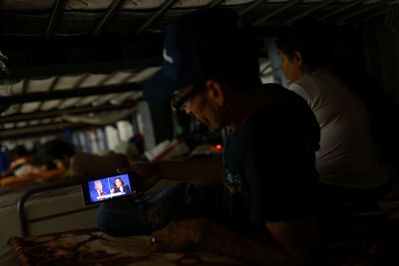 © Reuters. FILE PHOTO: A migrant, seeking to reach the United States and request asylum, watches the presidential debate between the Republican presidential nominee, former U.S. President Donald Trump and the Democratic presidential nominee, U.S. Vice President Kamala Harris, on a mobile phone screen inside the El Buen Samaritano shelter in Ciudad Juarez, Mexico, September 10, 2024. REUTERS/Jose Luis Gonzalez/File photo