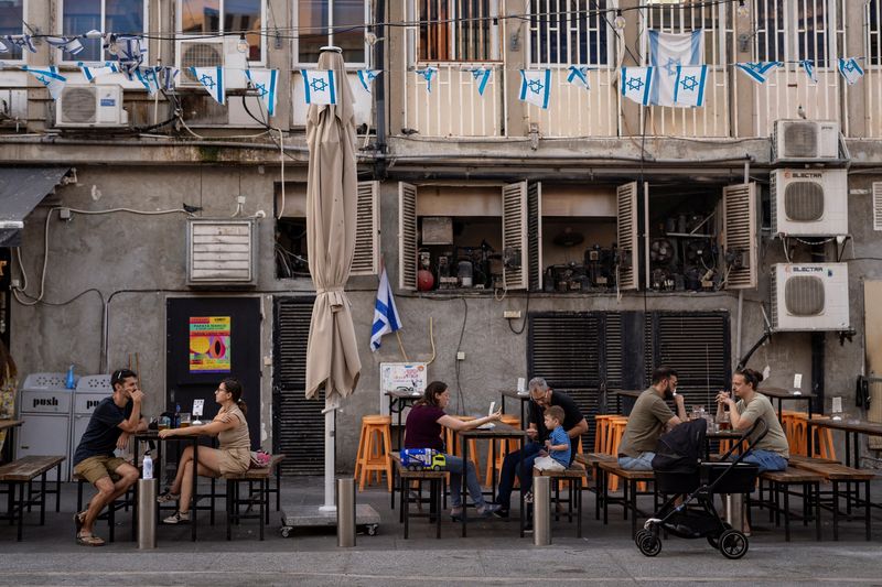 People sit at an outdoor restaurant with Israeli flags in Tel Aviv during the conflict, July 12, 2024.  Reuters