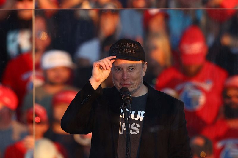 © Reuters. FILE PHOTO: Tesla CEO and X owner Elon Musk gestures behind protective glass during a rally for Republican presidential nominee and former U.S. president Donald Trump, at the site of the July assassination attempt against Trump, in Butler, Pennsylvania, U.S., October 5, 2024. REUTERS/Carlos Barria/File Photo