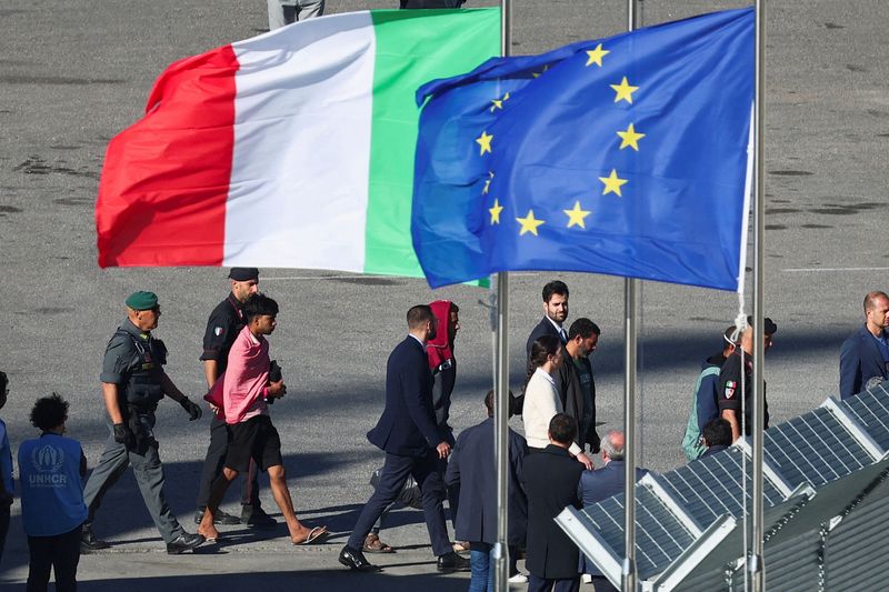 &copy; Reuters. Migrants and security officials walk next to the European Union flag and Italian flag as they disembark from the Italian navy ship Libra that arrived in Albania as part of a deal with Italy to process thousands of asylum-seekers caught near Italian waters