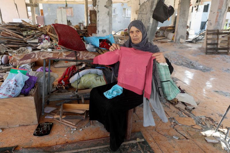 &copy; Reuters. Zakeya Al-Wasifi, avó de cinco crianças palestinas mortas em um ataque israelense, mostra roupas dos netos dentro da casa danificada da família em Nuseirat, na Faixa de Gazan15/10/2024nREUTERS/Ramadan Abed