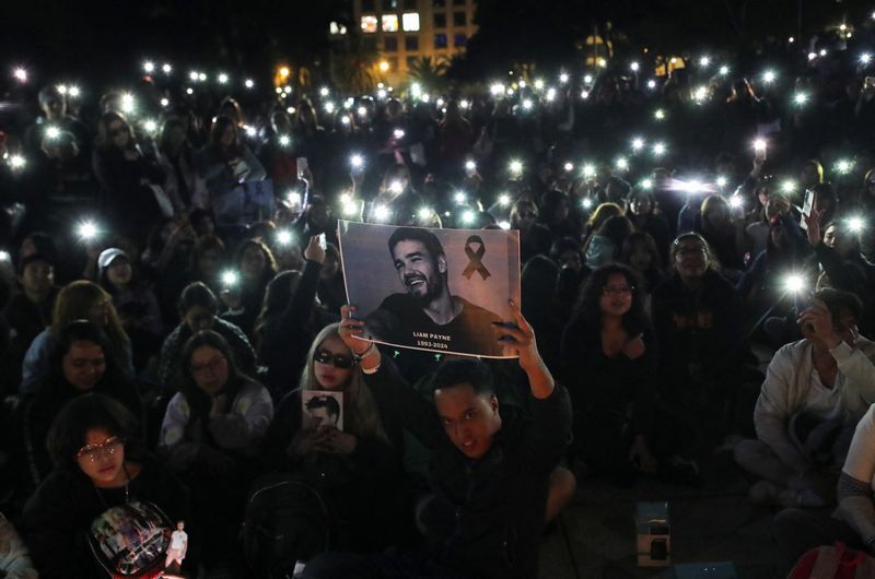 © Reuters. A man holds a poster with an image of Liam Payne next to One Direction fans as they gather to pay tribute to Liam Payne, at the Monument of the Revolution, in Mexico City, Mexico October 17, 2024. REUTERS/Henry Romero