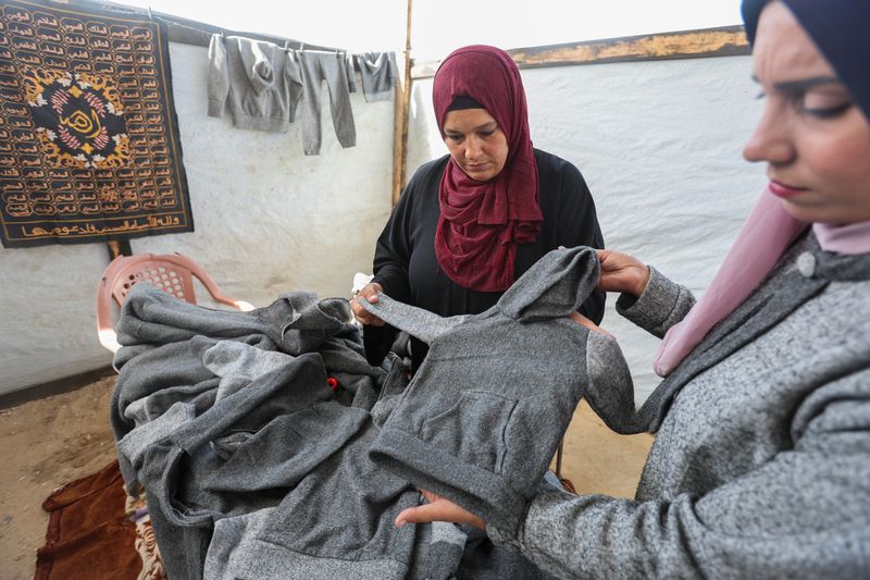 &copy; Reuters. Palestinian Nidaa Attia (R) and another woman display winter clothes they sewed for displaced people from from blankets, amid clothing shortages, at a tent in Khan Younis in the southern Gaza Strip, October 26, 2024. REUTERS/Ramadan Abed