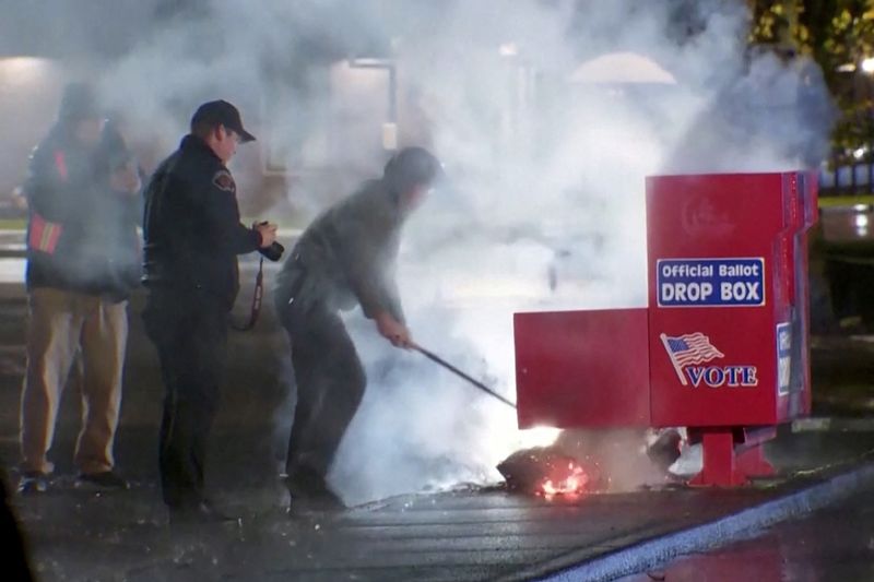 © Reuters. First responders pull out the burning contents of a ballot box, used to collect early votes ahead of the Nov. 5 U.S. election, after it was set on fire in a suspected arson in Vancouver, Washington, U.S. October 28, 2024 in a still image from video.  Evan Bell/ABC Affiliate KATU via REUTERS       