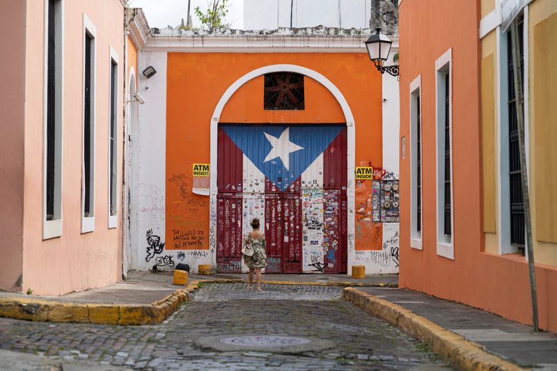 © Reuters. A woman takes photos of a gate with the Puerto Rican flag painted on it, in Old San Juan, Puerto Rico, October 28, 2024. REUTERS/Ricardo Arduengo