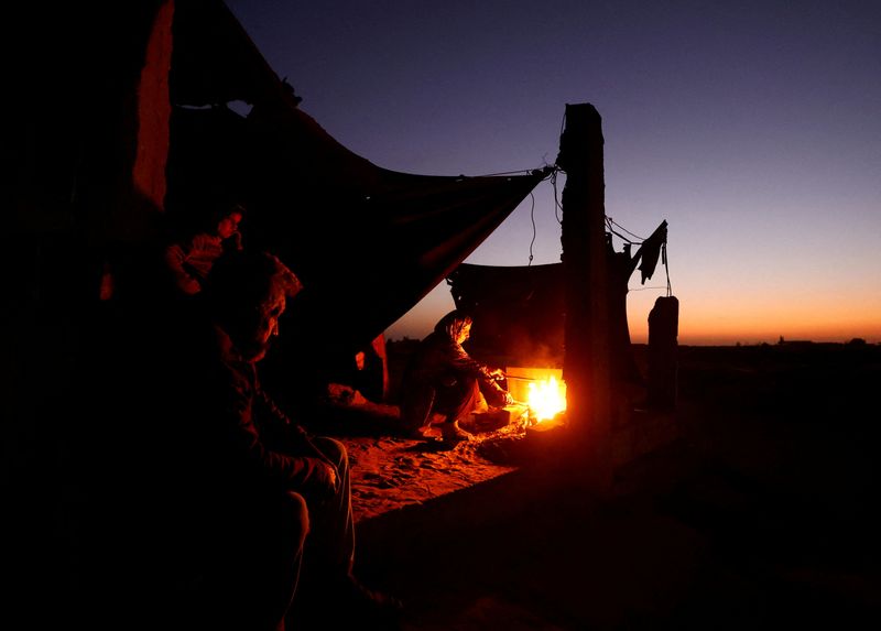 © Reuters. Displaced Palestinian woman Ghada Al-Aassas and her husband Abu Razzak sit by a fire as they shelter within a cemetery, amid the Israel-Hamas conflict, in Khan Younis, in the southern Gaza Strip, October 27, 2024. REUTERS/Mohammed Salem