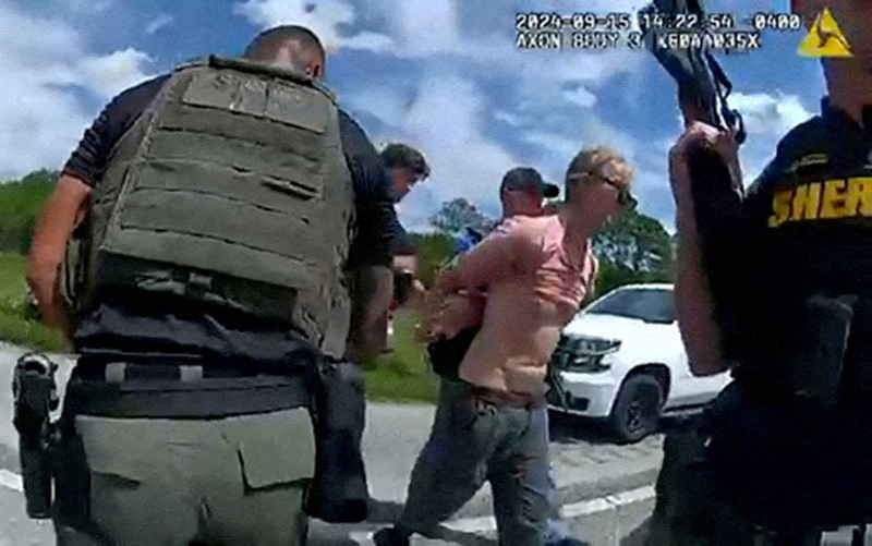 © Reuters. FILE PHOTO: Ryan W. Routh, suspected of attempting to assassinate Republican presidential nominee and former U.S. President Donald Trump at his West Palm Beach golf course, is led by two Martin County Sheriff's Office deputies after his arrest during a traffic stop near Palm City, Florida, U.S., September 15, 2024 in a still image from body camera video.  Martin County Sheriff's Office/Handout via REUTERS  