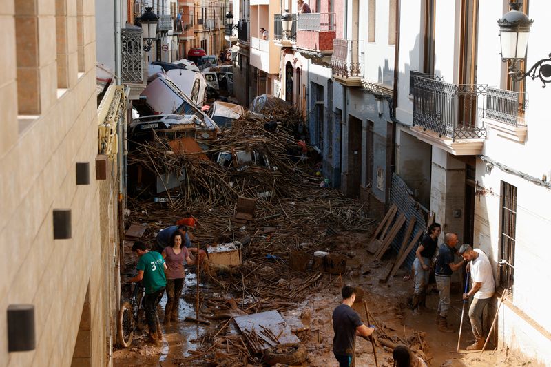 © Reuters. People work to clear a mud-covered street with piled up cars in the aftermath of torrential rains that caused flooding, in Paiporta, Spain, October 31, 2024. REUTERS/Eva Manez