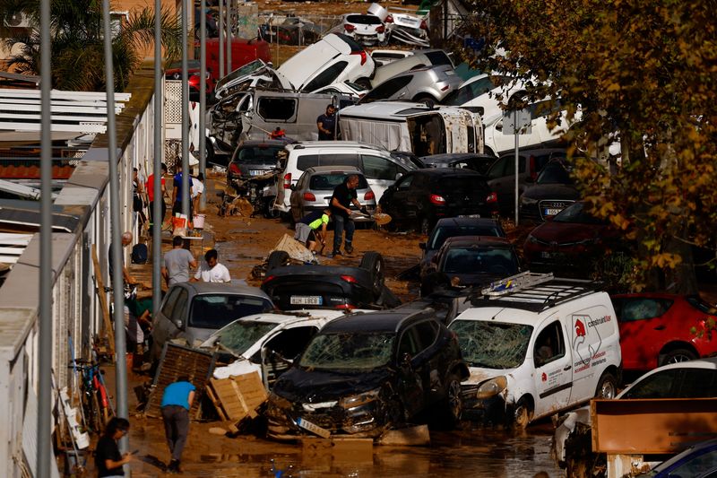 © Reuters. People clean up a mud-covered street next to piled up cars after heavy rains in Alfafar, in Valencia, Spain, November 1, 2024. REUTERS/Susana Vera