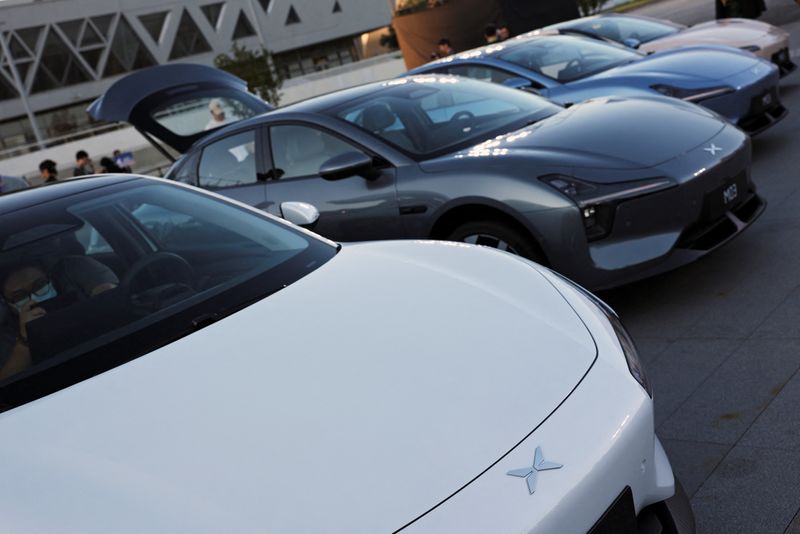 © Reuters. FILE PHOTO: Visitors look at MONA M03 electric vehicles (EV), displayed outside the venue of XPeng's launch event, in Beijing, China August 27, 2024. REUTERS/Florence Lo/File Photo