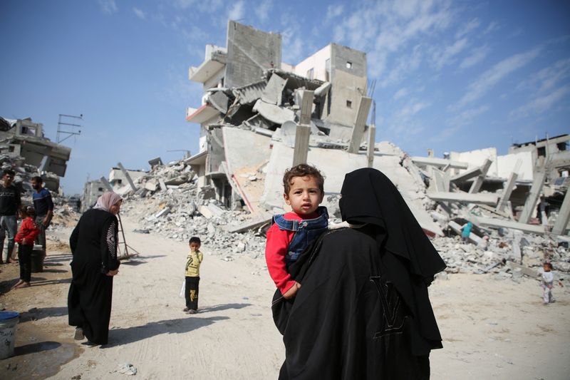 © Reuters. A Palestinian woman carries a child as they walk past the rubble of houses destroyed in previous strikes during the Israeli military offensive, amid the Israel-Hamas conflict, in Khan Younis in the southern Gaza Strip November 6, 2024. REUTERS/Hatem Khaled      