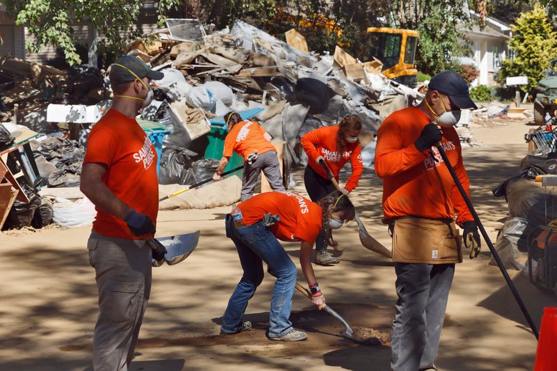 © Reuters. Volunteers from a Christian aid organization sweep dirt from a road in front of piles of trash after the previously flooded interiors of homes were cleaned and stripped of ruined materials two weeks after Hurricane Helene struck, in Swannanoa, North Carolina, U.S. October 11, 2024. REUTERS/Jonathan Drake/ File Photo