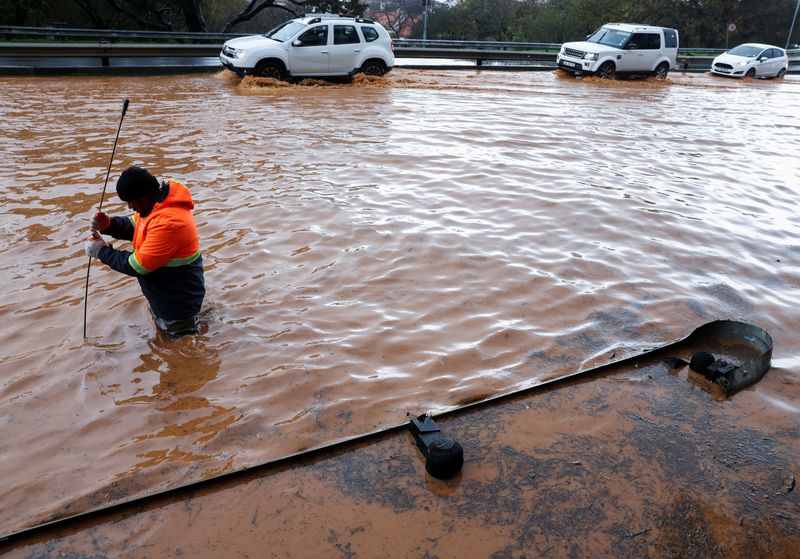 © Reuters. FILE PHOTO: A municipal worker attempts to unclog a flooded road in Newlands during heavy rains in Cape Town, South Africa, July 9, 2024. REUTERS/Esa Alexander/File Photo