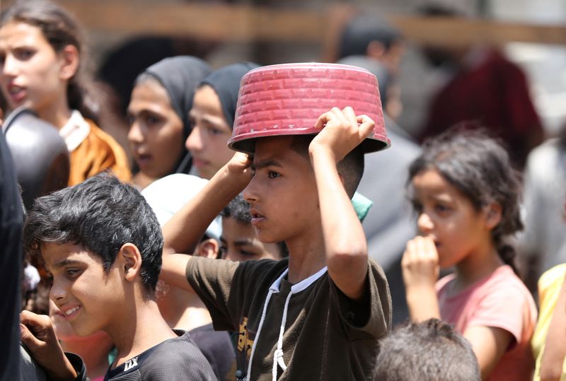 © Reuters. FILE PHOTO: Palestinians gather to receive food cooked by a charity kitchen, amid shortages of aid supplies, as the conflict between Israel and Hamas continues, in Khan Younis, in the southern Gaza Strip, June 19, 2024. REUTERS/Hatem Khaled/File Photo