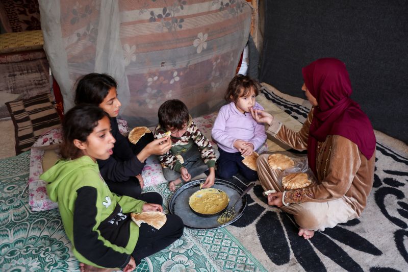 © Reuters. Itimad Al-Qanou, a displaced Palestinian mother from Jabalia, eats with her children inside a tent, amid Israel-Gaza conflict, in Deir Al-Balah, central Gaza Strip, November 9, 2024. REUTERS/Ramadan Abed