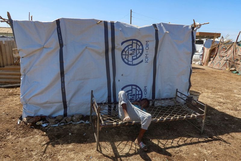 © Reuters. FILE PHOTO: A boy displaced from Sudan's Gezira state due to Rapid Support Forces violence, lies down on a bench with the logo of the International Organization for Migration in New Halfa, Sudan, November 2, 2024. REUTERS/El Tayeb Siddig/File Photo