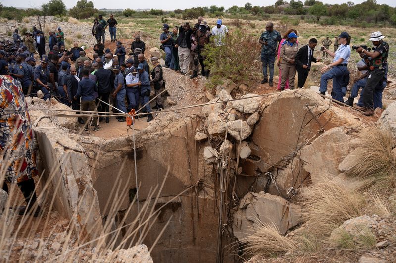 &copy; Reuters. Community members watch as Senzo Mchunu, South African police minister, inspects outside the mineshaft where it is estimated that hundreds of illegal miners are believed to be hiding underground, after police cut off food and water as part of police opera