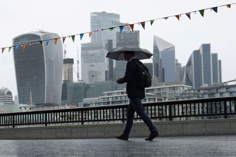 © Reuters. FILE PHOTO: A pedestrian carrying an umbrella walks along the River Thames in view of City of London skyline in London, Britain, July 31, 2023. REUTERS/Hollie Adams/File Photo