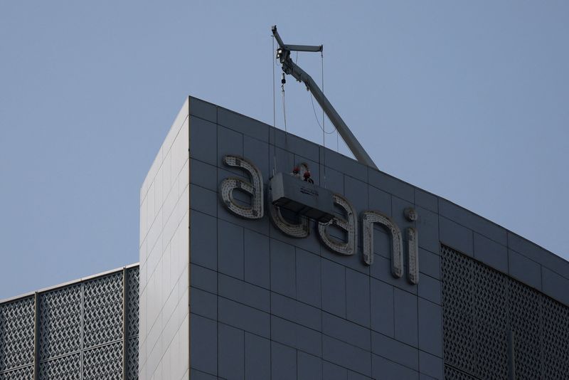 © Reuters. Men fix the Adani Group logo in front of its corporate house on the outskirts of Ahmedabad, India on November 21, 2024. REUTERS/Amit Dave