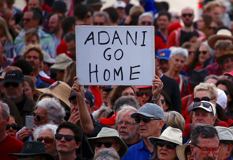 © Reuters. FILE PHOTO: A protester holds a sign as he participates in a national Day of Action against the Indian mining company Adani's planned coal mine project in north-east Australia, at Sydney's Bondi Beach in Australia, October 7, 2017.      REUTERS/David Gray/File Photo